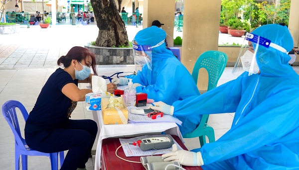 Một chị lấy giấy chứng nhận đã tiêm, bên kia là những người đang làm thủ tục chờ tiêm
